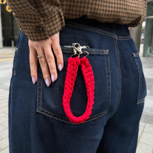 Person wearing a plaid shirt and blue jeans with a red knitted pouch in their back pocket on a city street.